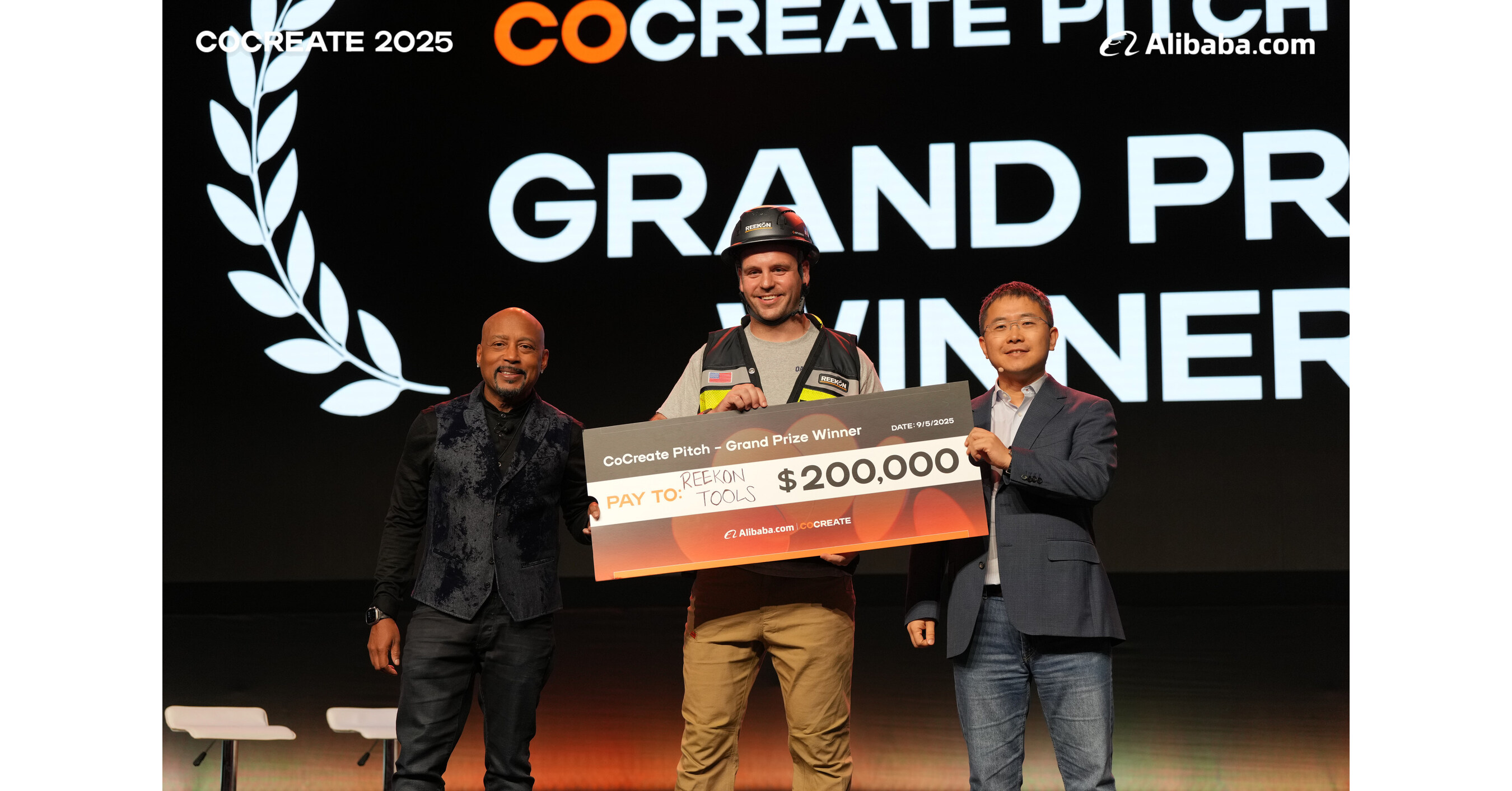 Christian Reed of Reekon Tools holding the $200,000 CoCreate Pitch Grand Prize check on stage alongside Daymond John at CoCreate 2025.